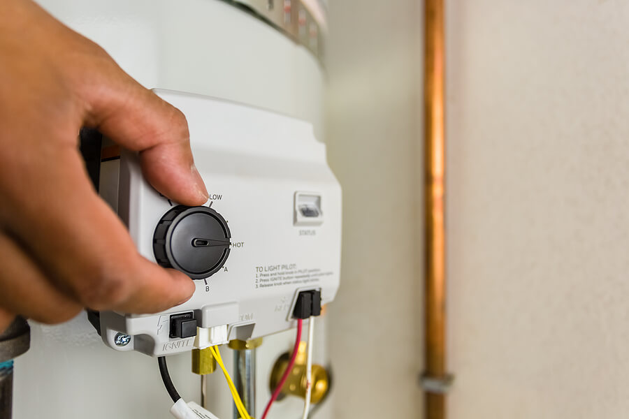 A Hand Turning A Black Knob On A White Water Heater.